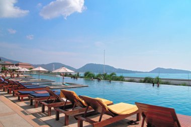 Dinlenmek için tatil kavramı. Otelde şemsiyeli ve güneşli havuzlu güzel bir açık havuz. Arka planda mavi gökyüzü ve deniz. 