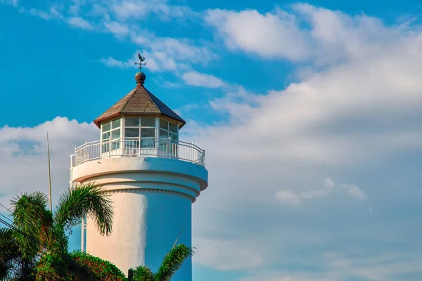 White retro lighthouse on the tropical coast. Bottom view. On blue sky background with white clouds. Copy space. — Stock Photo, Image