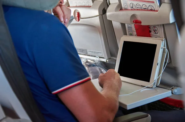 El hombre usa una tableta en un avión de pasajeros. Tableta con una pantalla en blanco y negro . — Foto de Stock