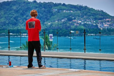 Arkadan görünüş portresi bir genç adam açık havuzun kenarında duran ve akıllı telefon kullanarak. Kopya alanı.