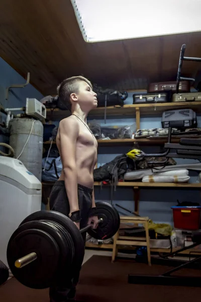Мальчик поднимает штангу в гараже. Силовая подготовка на дому, подъем тяжестей — стоковое фото