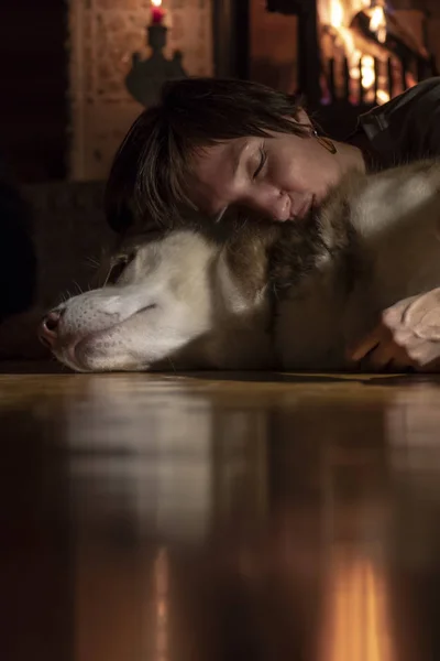 Mujer descansa la cabeza sobre el perro y duerme en habitación oscura con chimenea. Confort, amor y cuidado —  Fotos de Stock