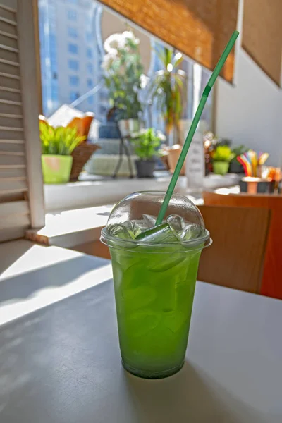 Tarragon lemonade with ice cubes in transparent plastic cup with straw.