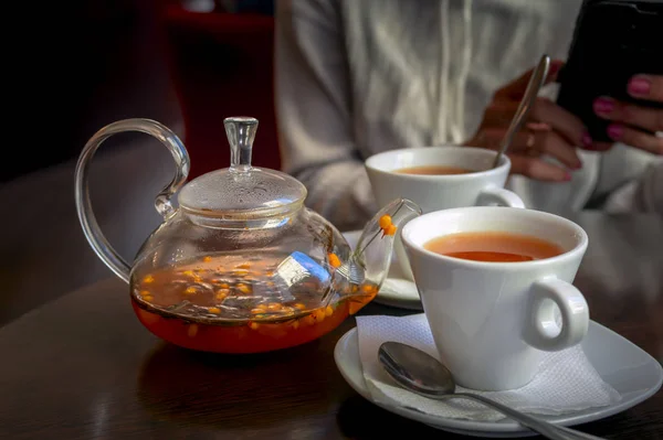 Thé d'argousier dans une théière en verre. Thé à base de plantes est versé dans des tasses blanches de théière en verre . — Photo