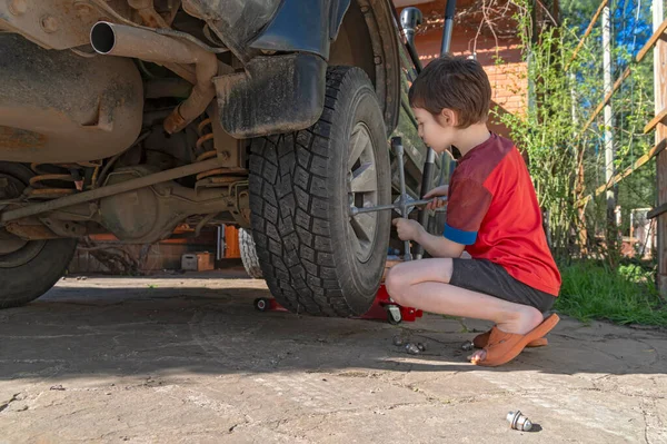 Portrait of little boy changing wheels on car with cross wheel wrench outside — Stock Photo, Image