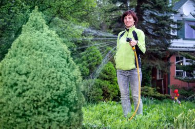 Ağaç bitkilerini sulayan gülümseyen kız. Bahçıvan su püskürtür..