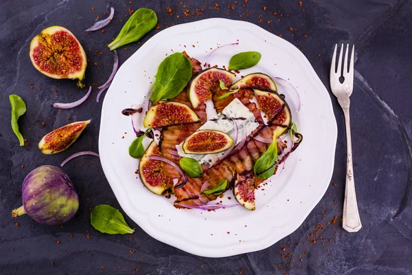 Инжир и жареный бекон с маленькими листьями салата подаются на белой тарелке. Итальянская кухня . — стоковое фото