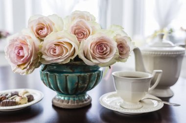 Fincan çay ve masada vintage bir vazoda güzel gül buketi. 