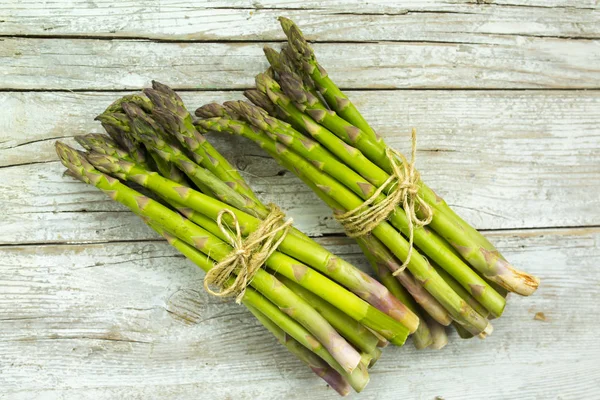 Ahşap bir arka plan üzerinde taze ve çiğ yeşil kuşkonmaz demet. 