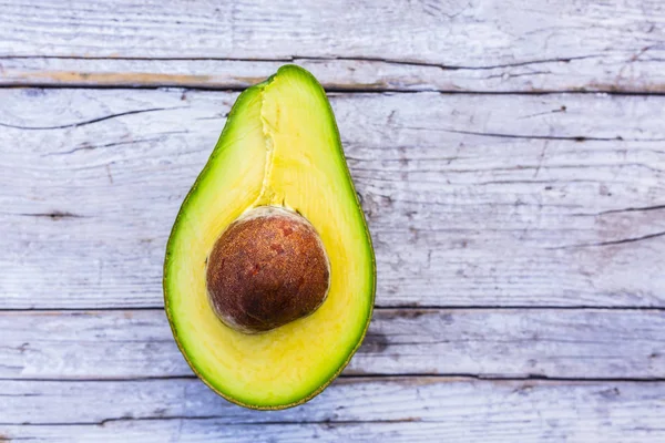 Ahşap bir arka planda avokadonun yarısı olgunlaşmış..