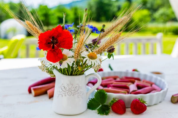 Bouquet of wild flowers and dessert with rhubarb and fresh strawberries on a wooden table in the garden.