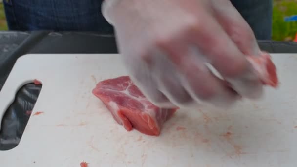 Hombre cortando la carne cruda en una pizarra blanca en un jardín — Vídeo de stock