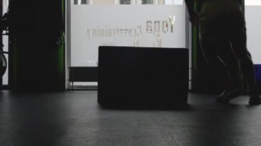 Formda genç adamın silueti egzersiz rutininin bir parçası olarak bir kutunun üzerine atlıyor. Spor salonunda zıplayan bir adam. Sporcu sandık atlayışı yapıyor.