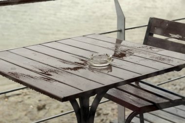 Masa, sandalye ve kül tablası manzaralı camına yağmur damlaları
