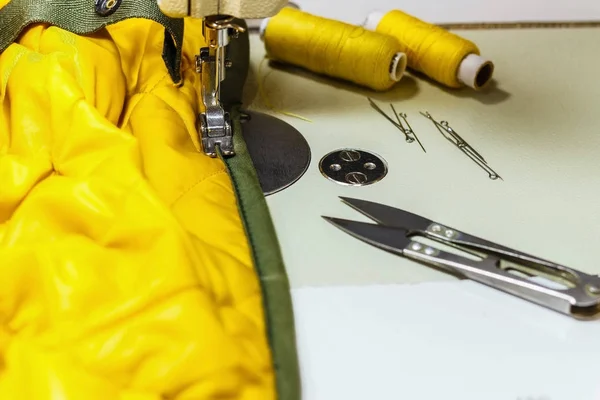 On the sewing machine is a yellow jacket, threads and scissors. — Stock Photo, Image