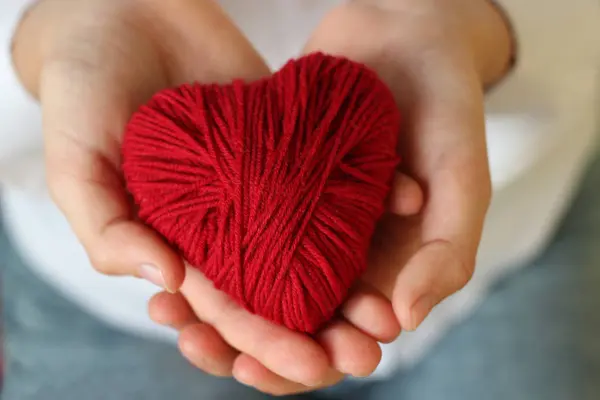 Le mani da bambini tengono un cuore di filo rosso per lavorare a maglia. Valente. — Foto Stock