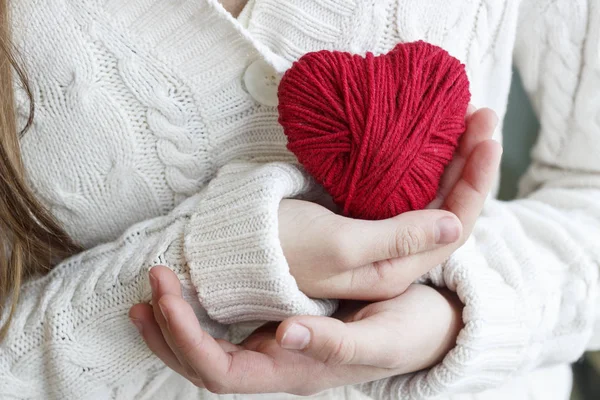 Kinderhände halten ein Herz aus rotem Faden zum Stricken. — Stockfoto