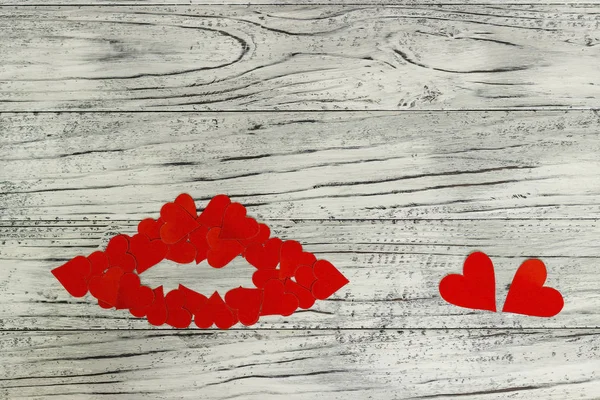 Lips of little red hearts on a wooden background. The concept of