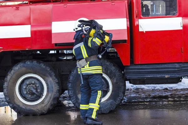 A fireman standing near a red fire engine and holding an oxygen