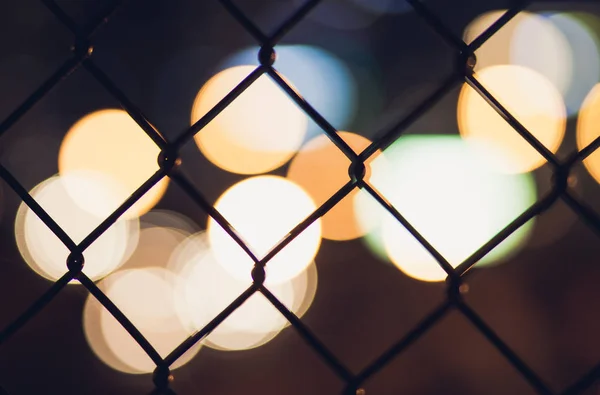 Nigh cidade bokeh luzes através da cerca de malha de arame — Fotografia de Stock