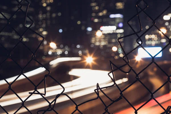 Nigh cidade bokeh luzes através da cerca de malha de arame — Fotografia de Stock