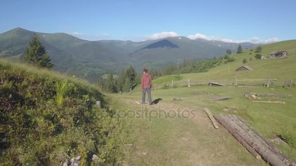 Drone voando sobre um homem caminhando no campo de montanha de grama verde alpina — Vídeo de Stock