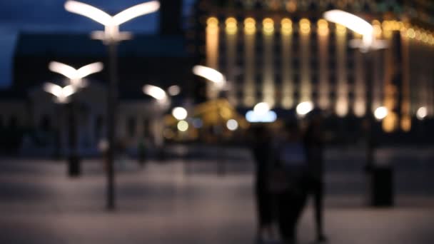 Fuera de foco fondo con borrosas luces desenfocadas de la ciudad y gente caminando en la plaza — Vídeo de stock