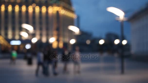 Fuera de foco fondo con borrosas luces desenfocadas de la ciudad y gente caminando en la plaza — Vídeo de stock