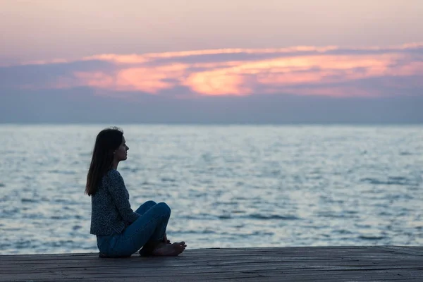 Ragazza sola seduta sulla spiaggia all'alba. Donna silhouette sopra — Foto Stock