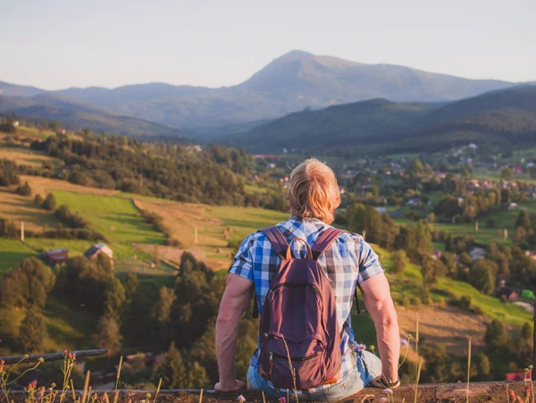 Caminhante com mochila sentada na cerca desfrutando de vista para a montanha — Fotografia de Stock