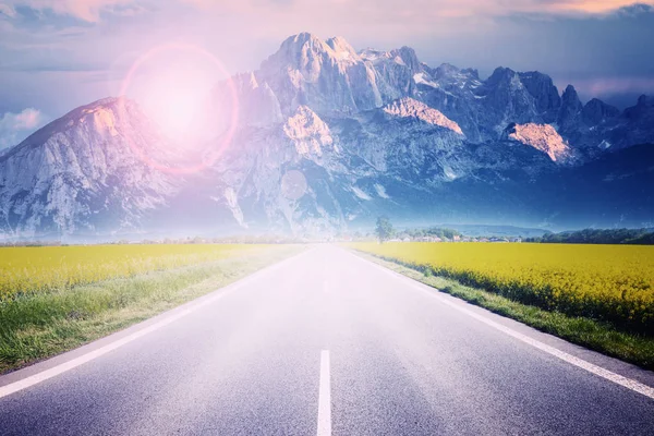 Rechte snelweg naar hoge bergen en een bewolkte hemel bij de zon — Stockfoto