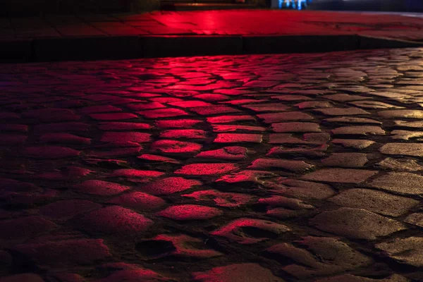 Mojado iluminado por la luz roja empedrado calle por la noche — Foto de Stock