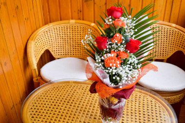 Saman yapılan sandalye yanında bir masaya serpiştirilmiş beyaz çiçek bir buket kırmızı ve Sarı Gül.