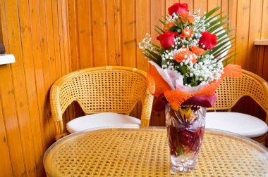 Saman yapılan sandalye yanında bir masaya serpiştirilmiş beyaz çiçek bir buket kırmızı ve Sarı Gül.