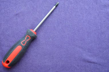 Kauçuk kırmızı-siyah kolu ve siyah ucu ile tornavida, mor bir arka planda Çapraz şekilli yarık. El metal iş aletleri.