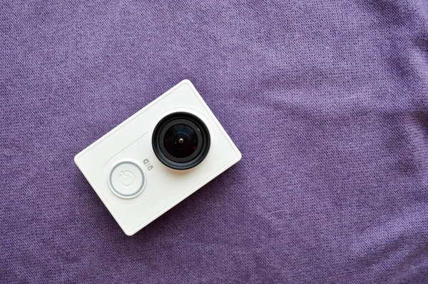 White action camera with a large black lens on a violet background
