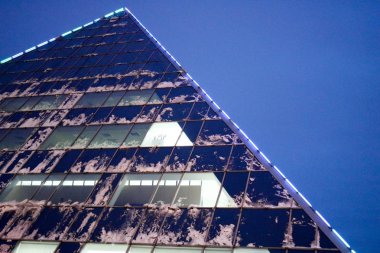 Üçgen, cam, ofis, aydınlık pencerelerin bulunduğu modern binanın köşesi, kış aylarında mavi bir gökyüzüne karşı geceleri karla kaplı bir gökdelen.