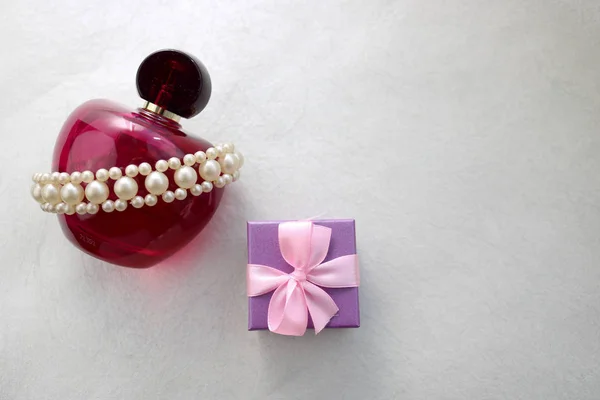 Pink beautiful glass transparent bottle of female perfume decorated with white precious pearls and blue small gift box and place for a simple text on a light white background.