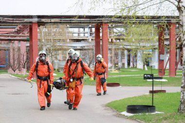 Dört profesyonel itfaiyeci itfaiye turuncu koruyucu yangına dayanıklı giysiler, beyaz kask ve gaz maskeleri sedye petrol rafinerisi tehlike bölgeden yaralı kişi devam