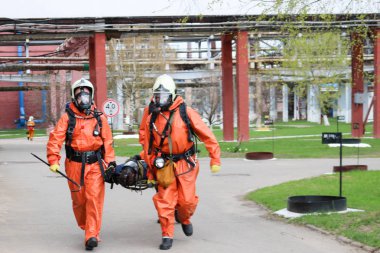 İki profesyonel itfaiyeci itfaiye turuncu koruyucu yangına dayanıklı giysiler, beyaz kask ve gaz maskeleri sedye Petrokimya tesisinde tehlike bölgesinden yaralı kişi devam
