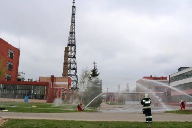Gaz maskesi ile beyaz kask turuncu ateşe dayanıklı elbiseli profesyonel itfaiye Yangın hortumlar test ve kimyasal Rafinerisi'nde yangın söndürmek için ateş.