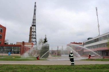 Gaz maskesi ile beyaz kask turuncu ateşe dayanıklı elbiseli profesyonel itfaiye Yangın hortumlar test ve kimyasal Rafinerisi'nde yangın söndürmek için ateş.
