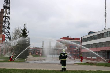 Gaz maskesi ile beyaz kask turuncu ateşe dayanıklı elbiseli profesyonel itfaiye Yangın hortumlar test ve kimyasal Rafinerisi'nde yangın söndürmek için ateş.