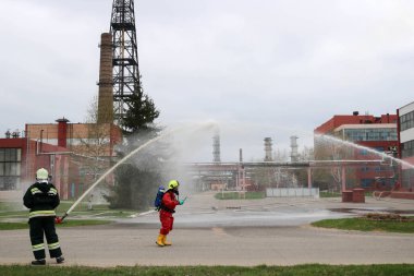 Gaz maskesi ile beyaz kask turuncu ateşe dayanıklı elbiseli profesyonel itfaiye Yangın hortumlar test ve kimyasal Rafinerisi'nde yangın söndürmek için ateş.