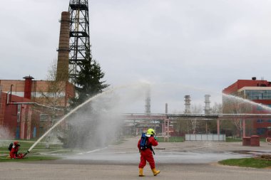 Gaz maskesi ile beyaz kask turuncu ateşe dayanıklı elbiseli profesyonel itfaiye Yangın hortumlar test ve kimyasal Rafinerisi'nde yangın söndürmek için ateş.