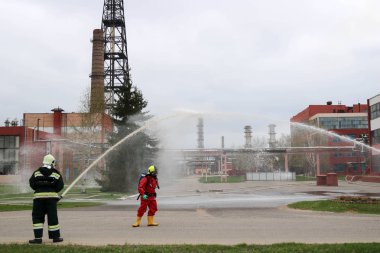 Gaz maskesi ile beyaz kask turuncu ateşe dayanıklı elbiseli profesyonel itfaiye Yangın hortumlar test ve kimyasal Rafinerisi'nde yangın söndürmek için ateş.
