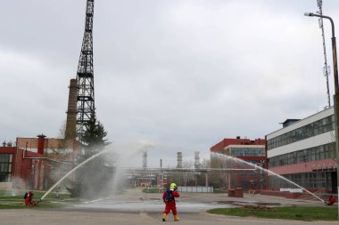 Gaz maskesi ile beyaz kask turuncu ateşe dayanıklı elbiseli profesyonel itfaiye Yangın hortumlar test ve kimyasal Rafinerisi'nde yangın söndürmek için ateş.