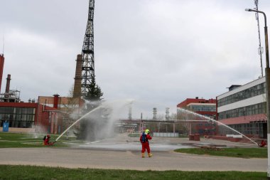 Gaz maskesi ile beyaz kask turuncu ateşe dayanıklı elbiseli profesyonel itfaiye Yangın hortumlar test ve kimyasal Rafinerisi'nde yangın söndürmek için ateş.