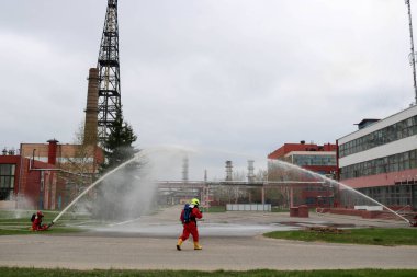 Gaz maskesi ile beyaz kask turuncu ateşe dayanıklı elbiseli profesyonel itfaiye Yangın hortumlar test ve kimyasal Rafinerisi'nde yangın söndürmek için ateş.