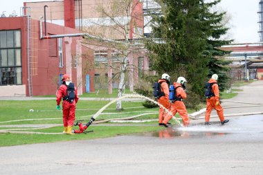 Gaz maskesi ile beyaz kask turuncu ateşe dayanıklı elbiseli profesyonel itfaiye Yangın hortumlar test ve kimyasal Rafinerisi'nde yangın söndürmek için ateş.